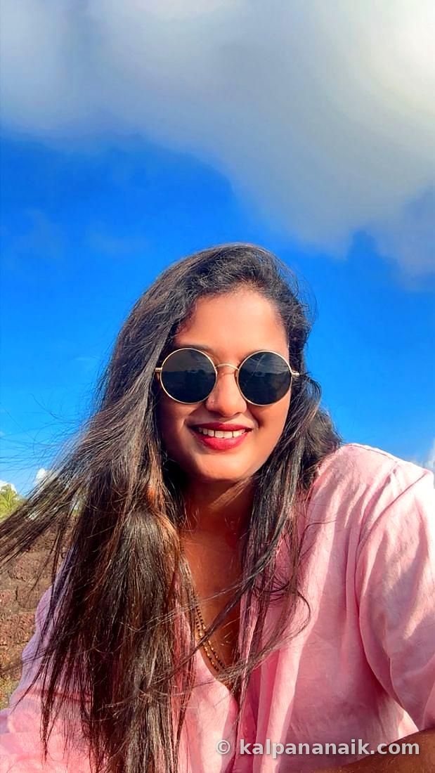 Kalpana smiling in round sunglasses under a bright blue sky